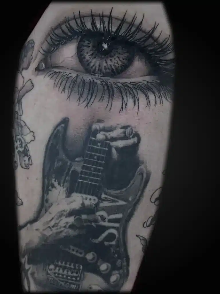 Black and gray eye and guitar realism tattoo by FIRME COPIAS Northwoods